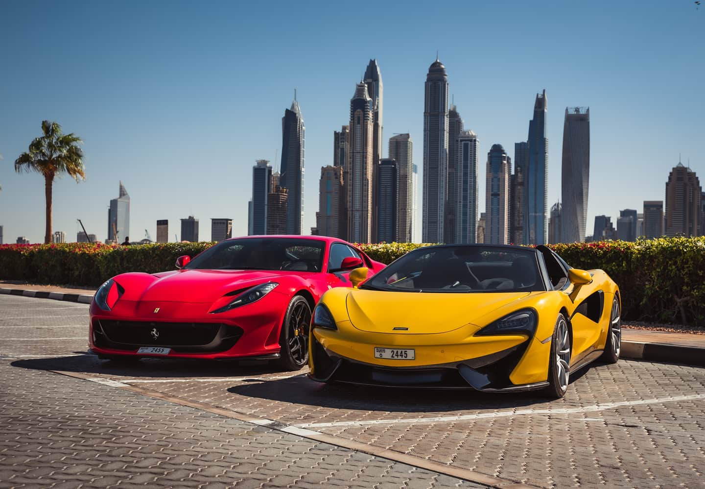 Red Ferrari and yellow McLaren parked with Dubai skyscrapers in the background.