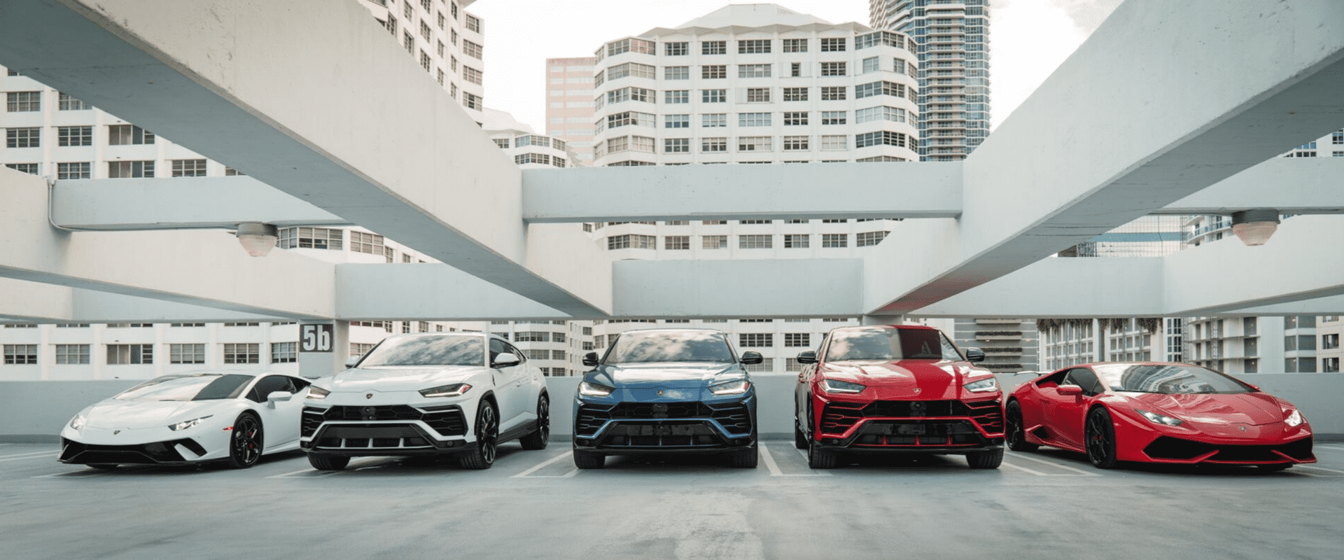 Two Lamborghini Huracans and three Lamborghini Uruses parked on a rooftop parking lot.