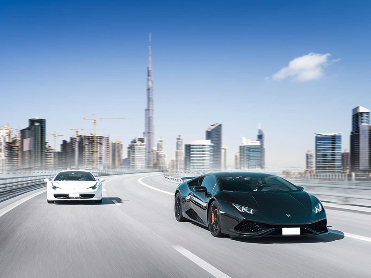 Luxury cars driving in Dubai, a black Lamborghini and a white Ferrari with the Burj Khalifa in the background